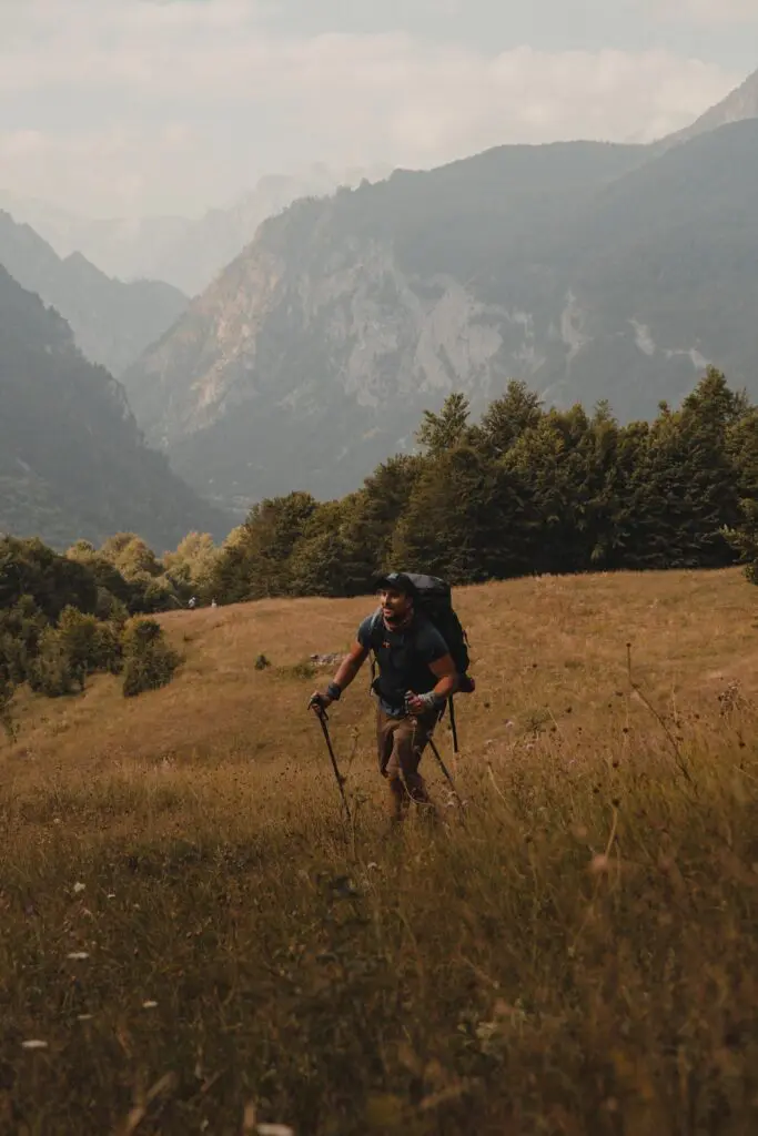 hiker with backpack and poles walking uphill in mountains