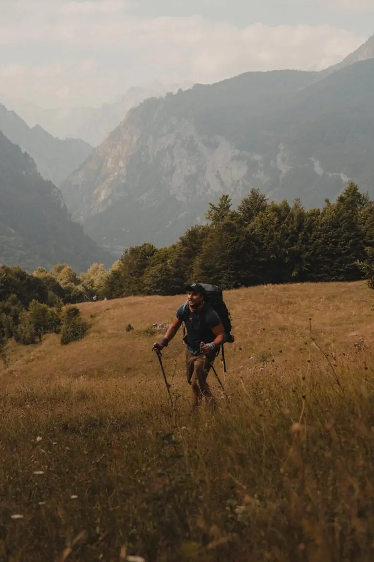 hiker with backpack and poles walking uphill in mountains