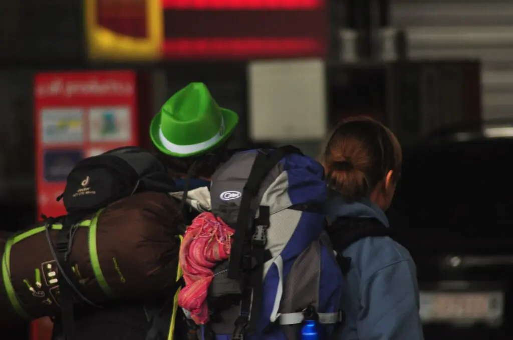 two travelers with backpacks, one wearing a green hat