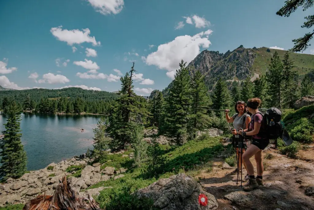 two women hiking by alpine lake with mountains